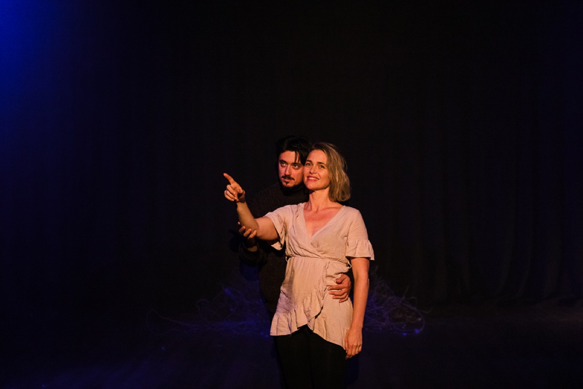 Two performers pointing outward together on a dark stage